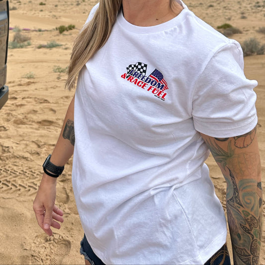 Person wearing a white t-shirt with freedom and race fuel logo, standing next to a truck in a desert landscape.