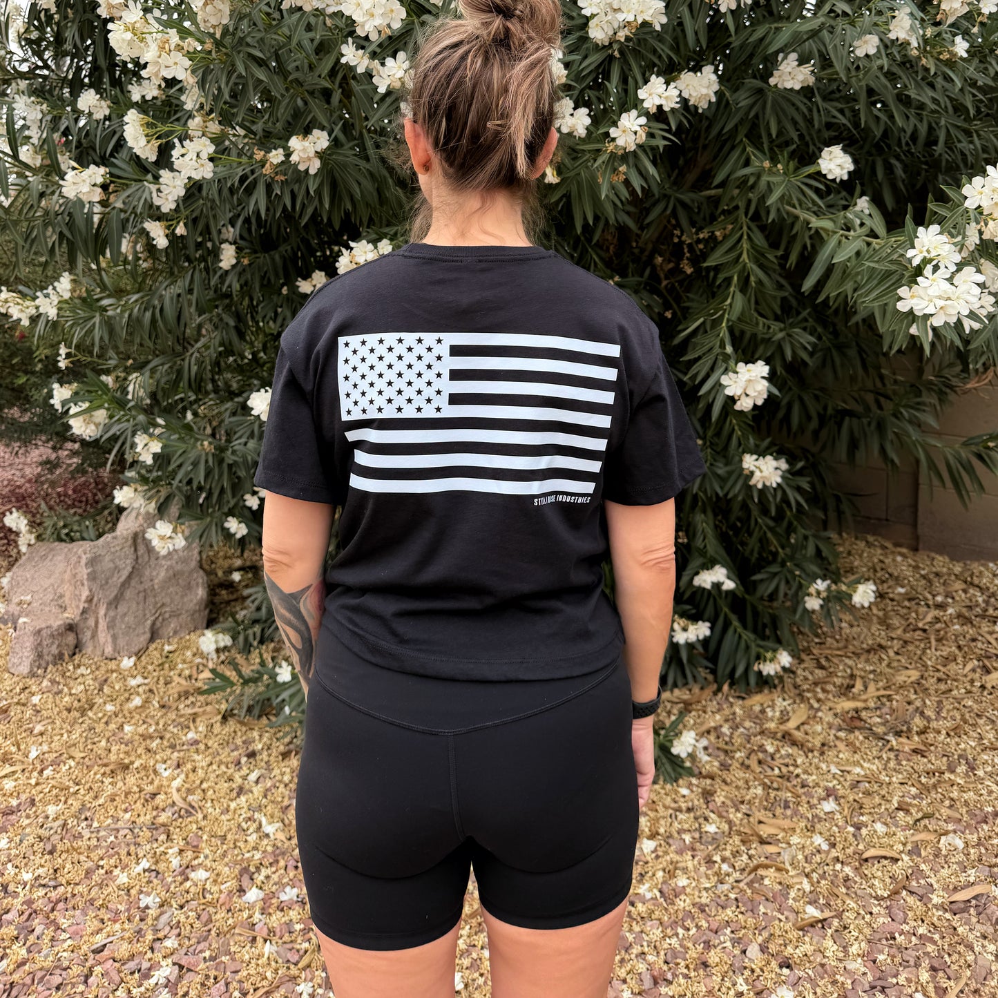 Person wearing a black t-shirt with a white flag design outdoors.